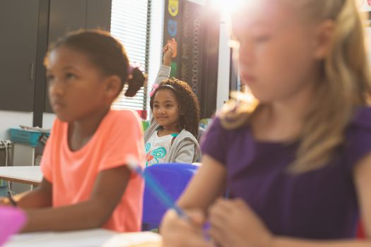 Schoolgirls sitting at desk in school and listening their teacher while a school girl raising hand in background