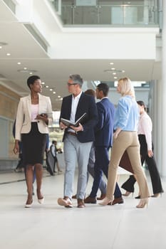 Front view of diverse business people interacting with each other while walking in lobby office