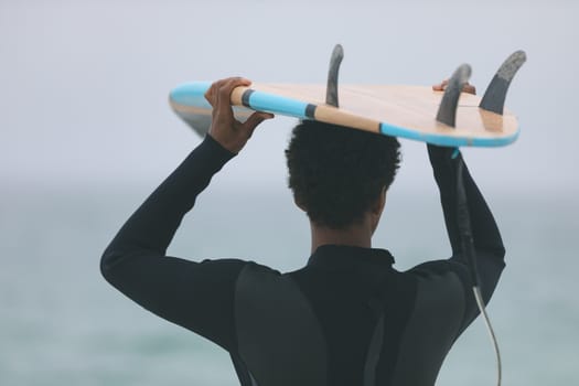 Rear view of young mixed-race male surfer carrying surfboard on her head at beach