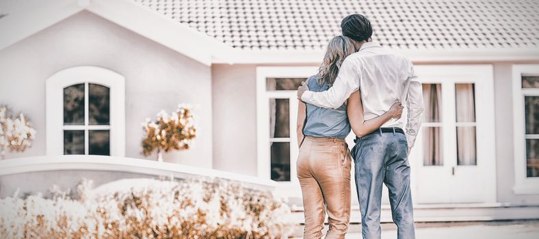 Rear view of couple standing with arm around outside the house