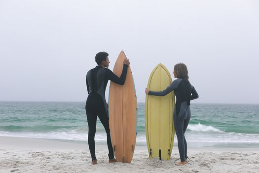 Rear view of young multi-ethnic couple surfer holding surfboards on the beach