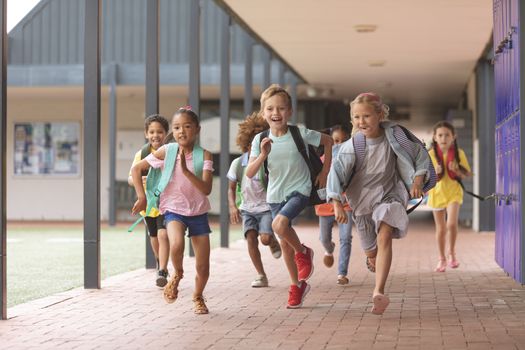 Front view of happy school kids running in corridor at school