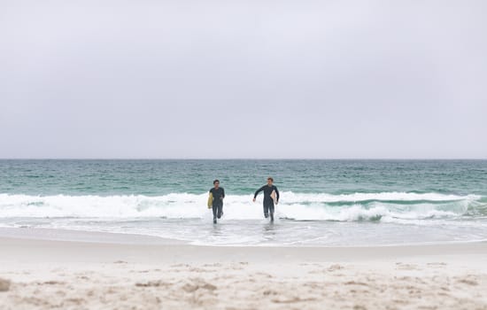 Front view of young multi-ethnic male friends running on beach while holding surfboards