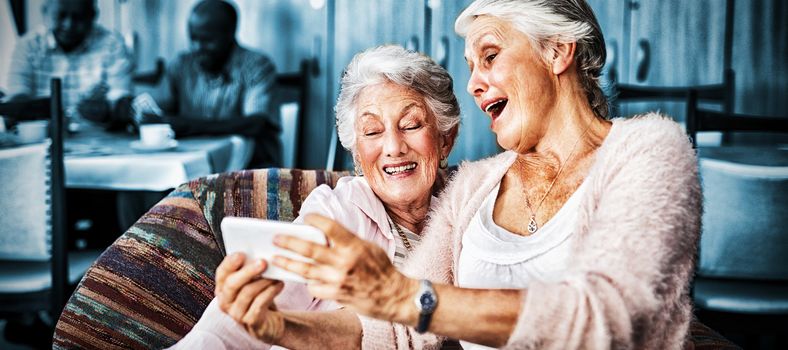 Senior friends taking selfie through smart phone while sitting on sofa at nursing home