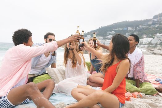 Front view of multi ethnic friends toasting with beer bottles on beach 