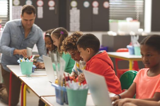 Side view of school kids using laptop in classroom while teacher teaching in background at school