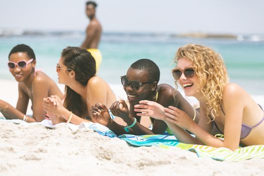 Front view of multi ethnic women interacting with each other while lying at beach on sunny day