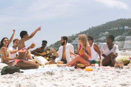 front view of multi ethnic group of friends relaxing and sitting on beach while interacting with each other