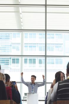Front view of young Asian businessman cheering while speaking in front of business professionals at seminar in office building