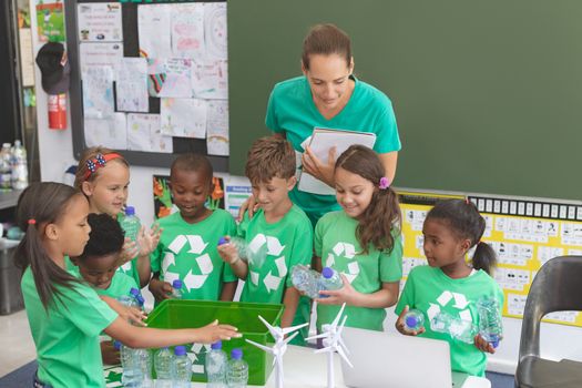 Front view of caucasian teacher and multi ethnic student discussing about green energy in classroom. Students holding plastic bottle