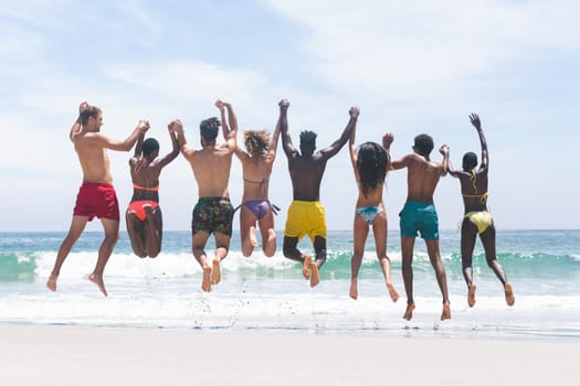 Rear view of diverse group friends enjoying and jumping in water at beach on a sunny day