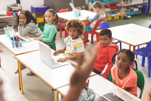 Front view of row of school kids listening their teacher in classroom at school while one of their classmates is drawing only on a table