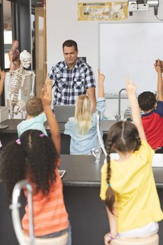 School kids raising hand while teacher asking question in classroom at school