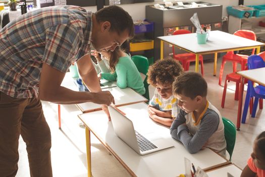 Side view of a teacher showing to his sdhool kids how use laptop in classroom at school