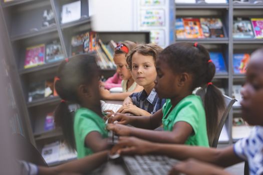 Portrait of happy Caucasian schoolboy sitting and looking at camera while others kids working on computer in computer room 