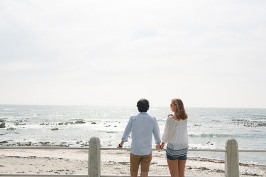 Rear view of young Caucasian couple standing hand in hand near sea side at promenade on a sunny day