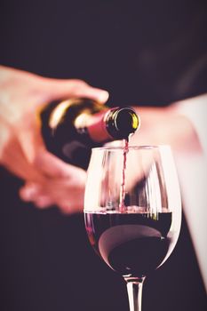 Mid section of waitress pouring red wine in a glass in restaurant