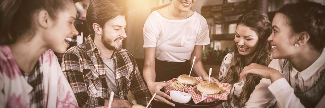 Young waitress serving burgers to customers in restaurant