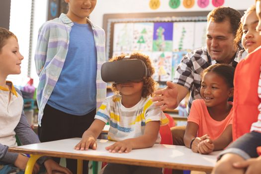 Front view of a schoolboy using virtual reality headset with his classmate and teacher at school
