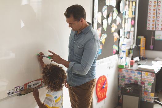 Side view of a Caucasian teacher teatching something to a metis school boy on a whiteboard agaisnt drawing in bacground