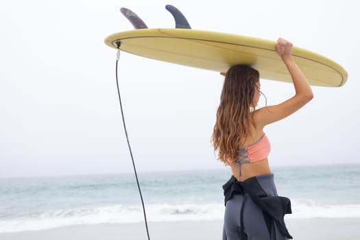 Rear view of young Caucasian female surfer carrying surfboard on her head at beach