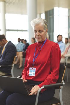 Front view of mature Caucasian businesswoman using laptop during seminar in office building