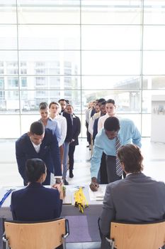 Front view of diverse business people checking in at conference registration table in office lobby