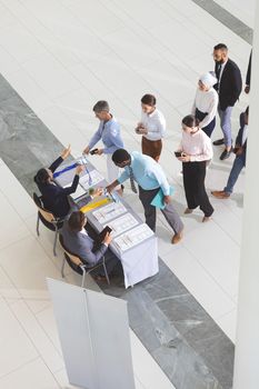 High angle view of diverse business people checking in at conference registration table in lobby 