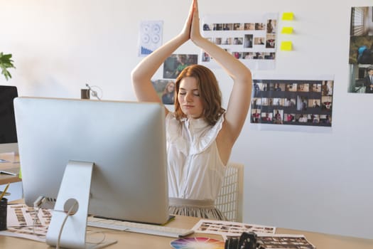 Front view of graphic designer with hand clasped doing yoga in creative office