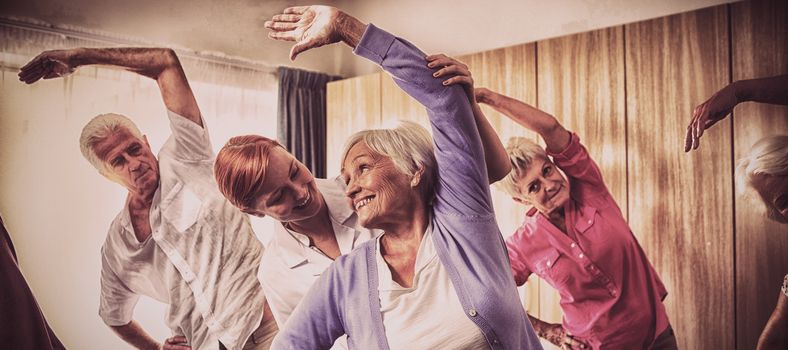Group of seniors doing exercises with nurse in retirement house