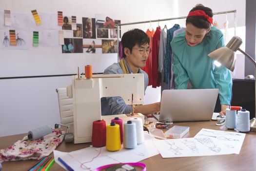 Front view of fashion designers discussing over laptop at desk in design studio 