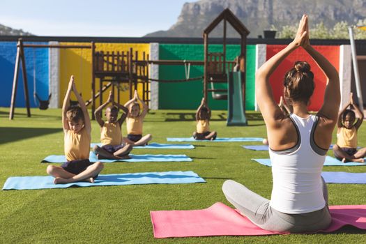 Front view of caucasian trainer teaching yoga to students on yoga mat in school playground at schoolyard