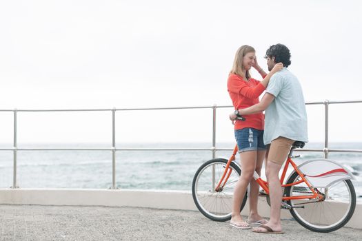 Side view of romantic young Caucasian couple embarrassing each other on cycle at beach. They are smiling 