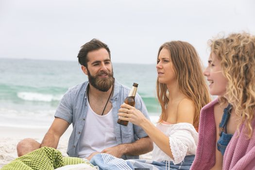 Front view of multi ethinc group of friends enjoying and interacting on beach while having beer 
