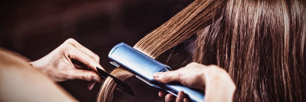 Female hairdresser straightening the hair of a client at a salon
