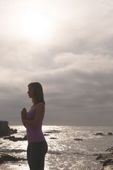 Side view of Caucasian blonde woman perform yoga on the beach. She is relaxed