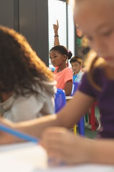 Front view of a schoolgirl raising hand while sitting in classroom at school