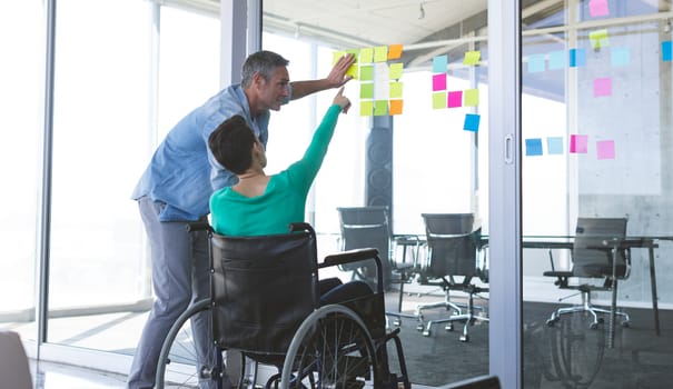 Business people discussing over sticky notes on glass wall in office
