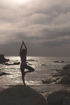 Rear view of Caucasian blonde woman perform yoga on the beach. She is relaxed