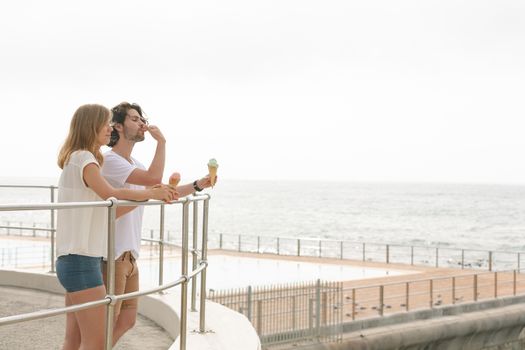 Side view of young Caucasian couple standing at promenade while having ice cream cone 