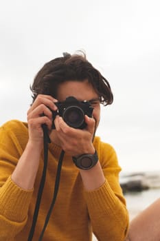 Front view of young Caucasian man using digital camera sitting on the beach 