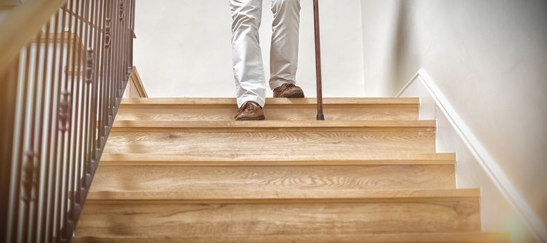 Senior man climbing downstairs with walking stick at home