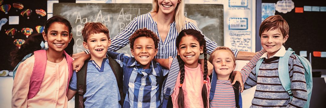 Happy teacher standing with schoolkids in classroom at school