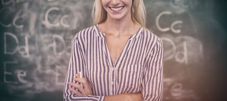 Portrait of happy teacher standing with arms crossed in classroom at school