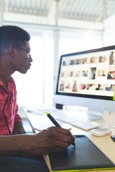 Side view of graphic designer working on graphic tablet and computer at desk in office