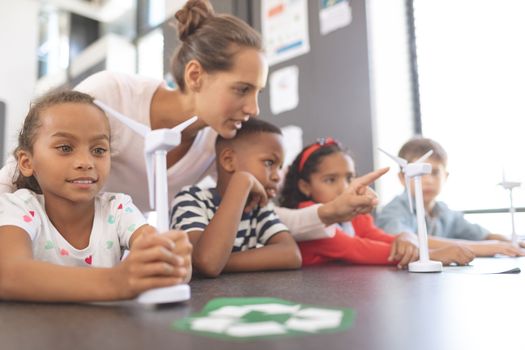 Side view of teacher explaining about windmill to school kids at school in classroom