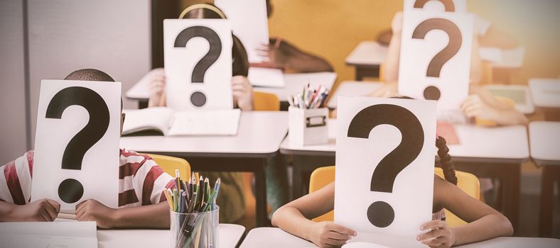 School kids covering their face with question mark sign in classroom at school