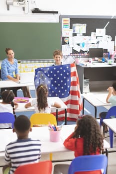 Front view of a schoolboy holding an american flag in classroom at school with his classmates in foreground