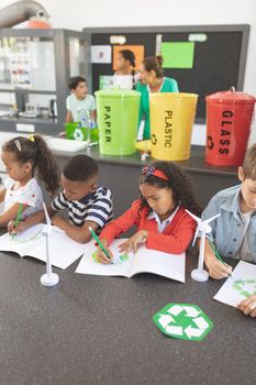 High angle view of school kids drawing on notebook in classroom with windmill mockup next to them against  trash cans plastic explosives of recycling in background