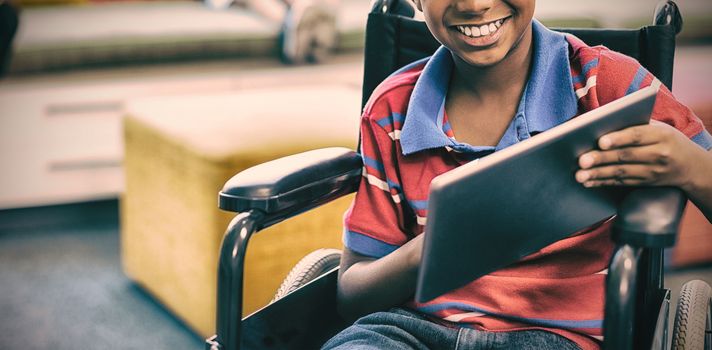 Portrait of disabled schoolboy on wheelchair using digital tablet in library at school